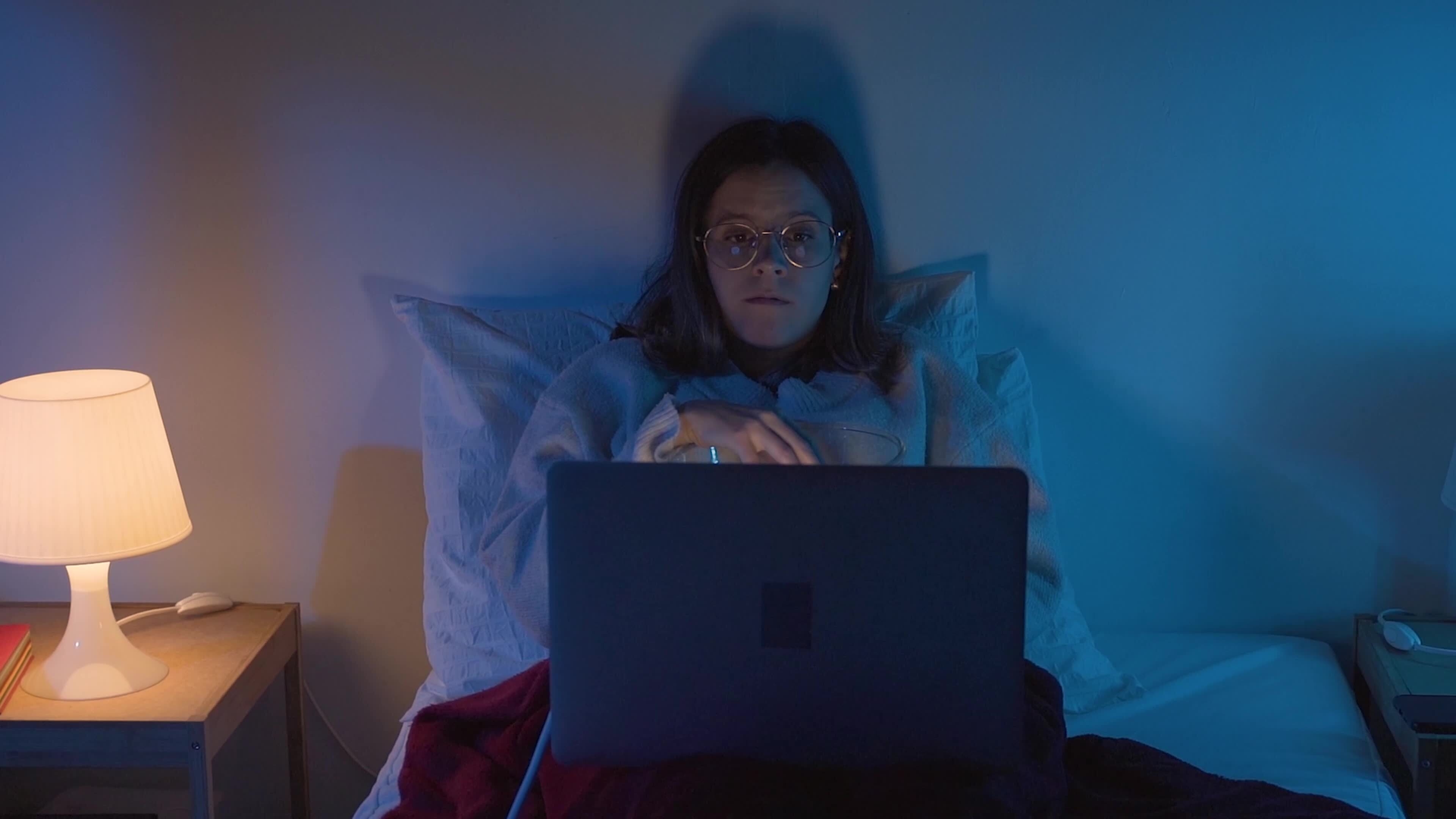 Young girl watching a movie eating popcorn with her laptop in bed at night.  Front view. Slow motion RED camera 4K 45732068 Stock Video at Vecteezy