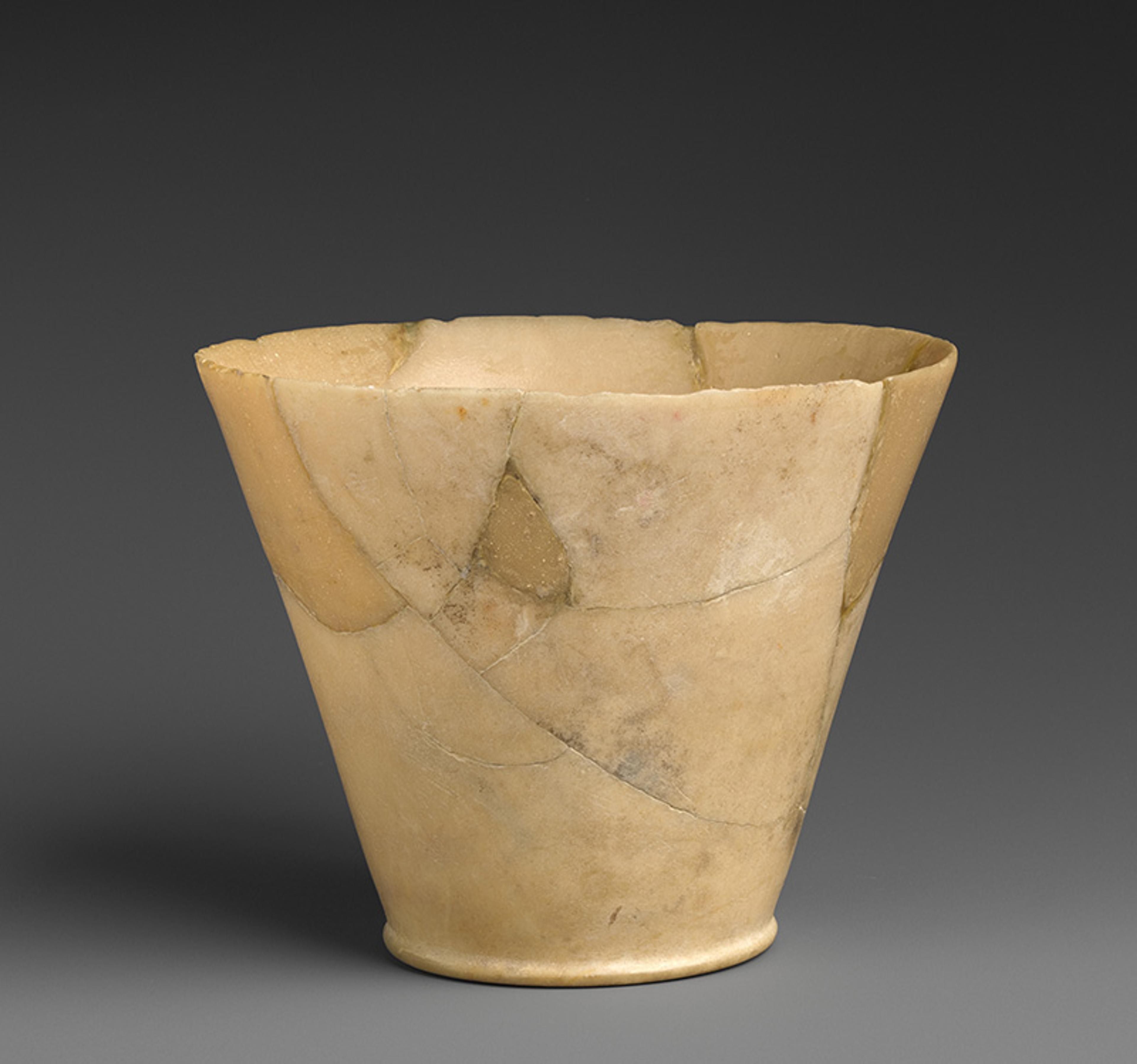 An ancient stone vessel with a conical shape on a plain dark background.