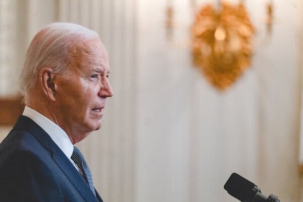 President Biden, wearing a blue jacket and tie and standing in front of a microphone.