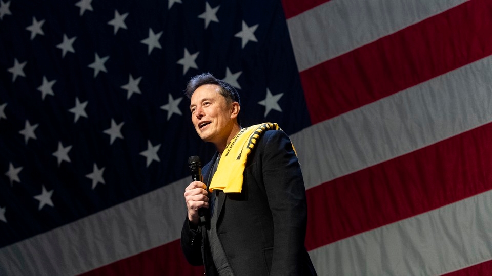 Elon Musk stands in front of a giant American flag