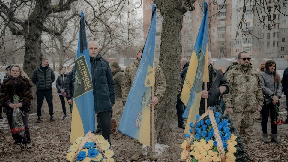 Ukrainian military men and civilians holding Ukrainian flags in a cemetery