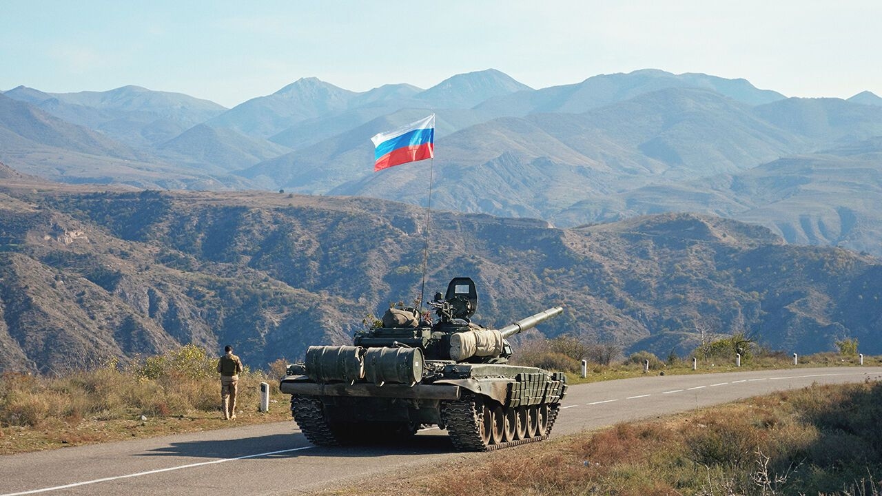 A service member of the Russian peacekeeping troops walks by a tank near the border with Armenia