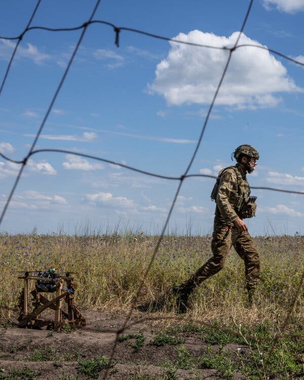 A man in fatigues, seen through netting, walking through a field. 
