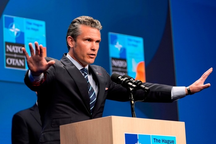 Pete Hegseth gestures with both hands while speaking at a podium