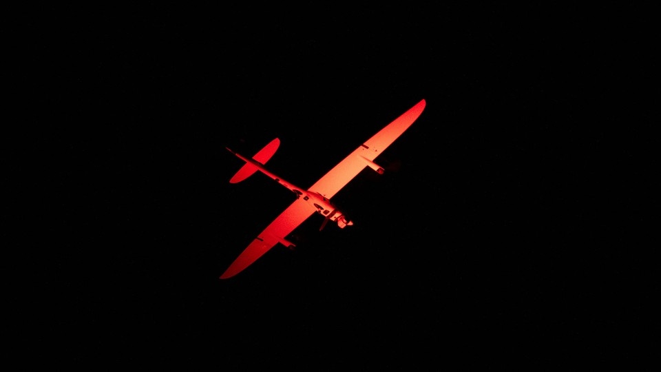 A plane in the pitch-black night sky is lit orange.
