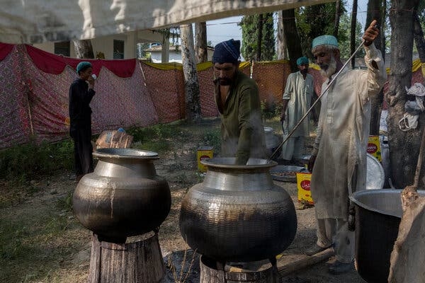 Two men stand over large cooking vessels outdoors.