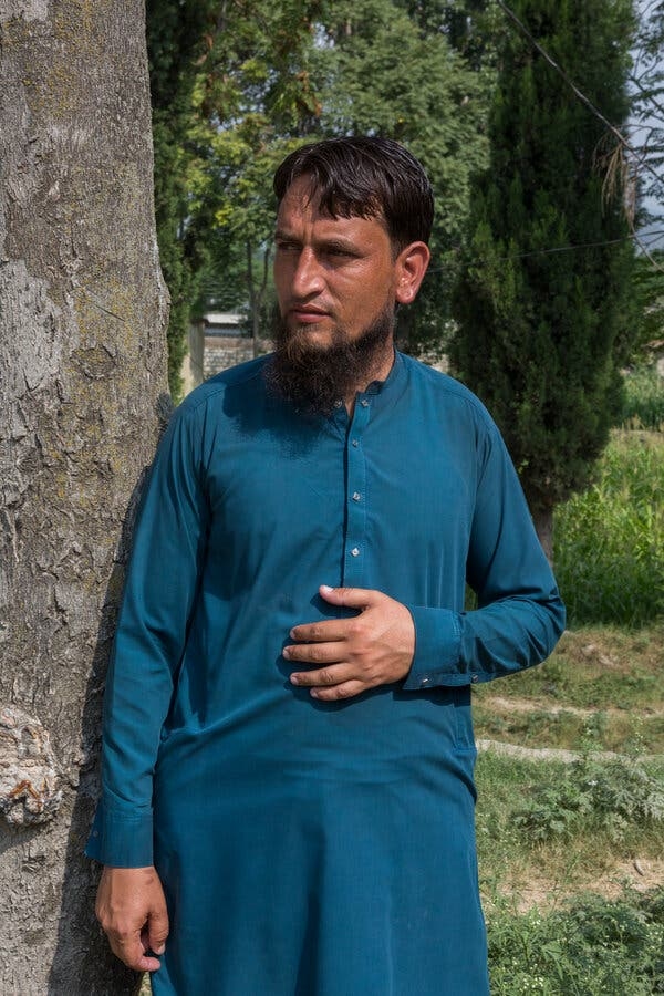 A man wearing a blue garb stands next to a tree.