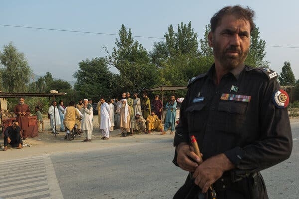 A policeman standing in a road with a line of people behind him.