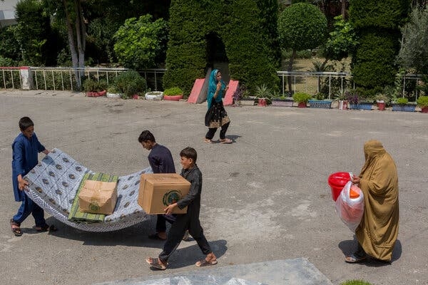 Three boys carrying bedding and boxes.