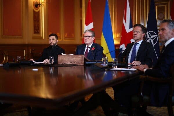 The four leaders sit at a large polished wooden table in an ornate hall.