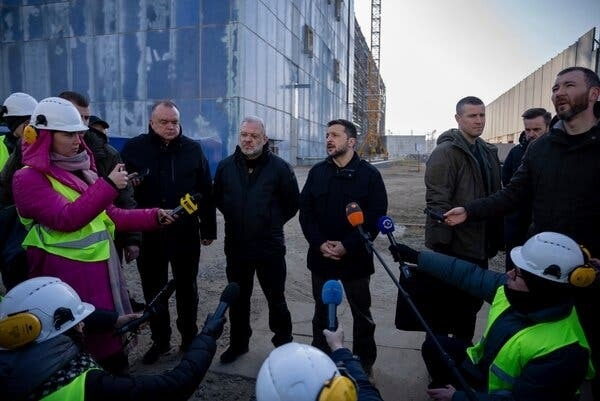 Volodymyr Zelensky, in a black coat, speaks to reporters.