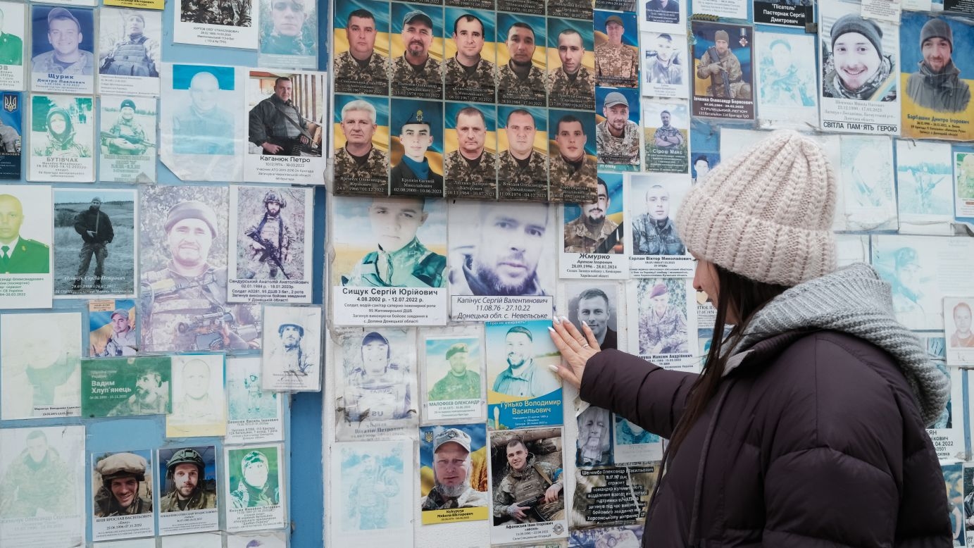 Oksana Borkun looks at the portrait of her husband displayed on a wall that honors Ukraine’s fallen soldiers in Kyiv.