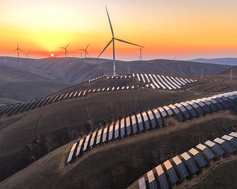 Wind turbines and rows of solar panels on rolling hills at sunset or sunrise