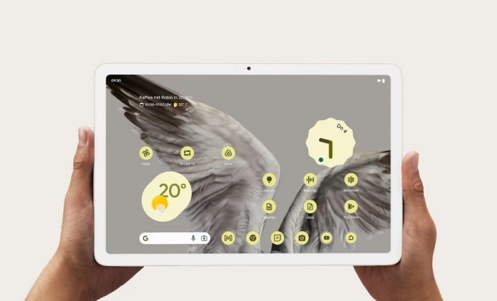 Zwei Hände, die Pixel Tablet halten, auf dessen Frontdisplay Wetter und Uhrzeit angezeigt werden.