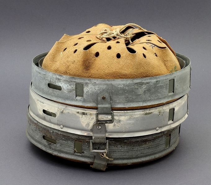 Three M31 liners stacked together. The liner in the middle has an aluminum band while the other two are zinc-coated steel. Note the chinstrap bale (D-ring) on the aluminum example; it is more square shaped than the others which have more rounded corners. Also this aluminum liner is a reinforced type; notice one of the supporting/reinforcing aluminum strips attached to the outer band with 4 small aluminum rivets. 