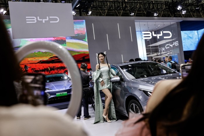 A Chinese model poses in front of a BYD Destroyer sedan at a car show