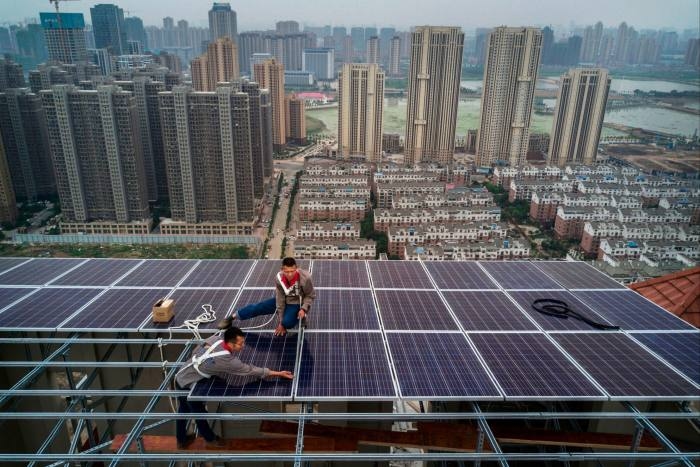Workers install solar panels on a new development with the skyline of Wuhan in the background