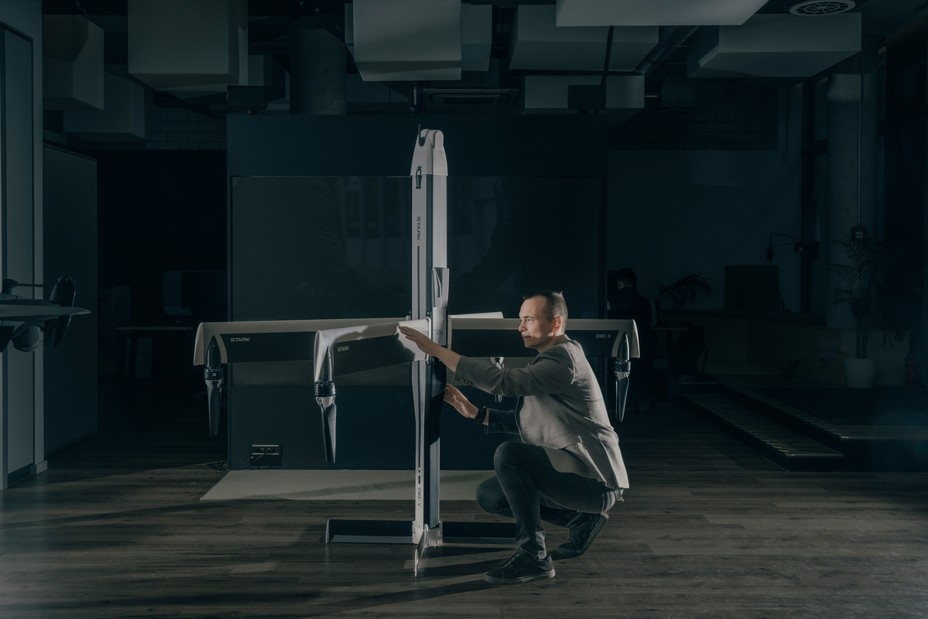 photo of man in suit crouching next to large multi-armed drone about twice his size