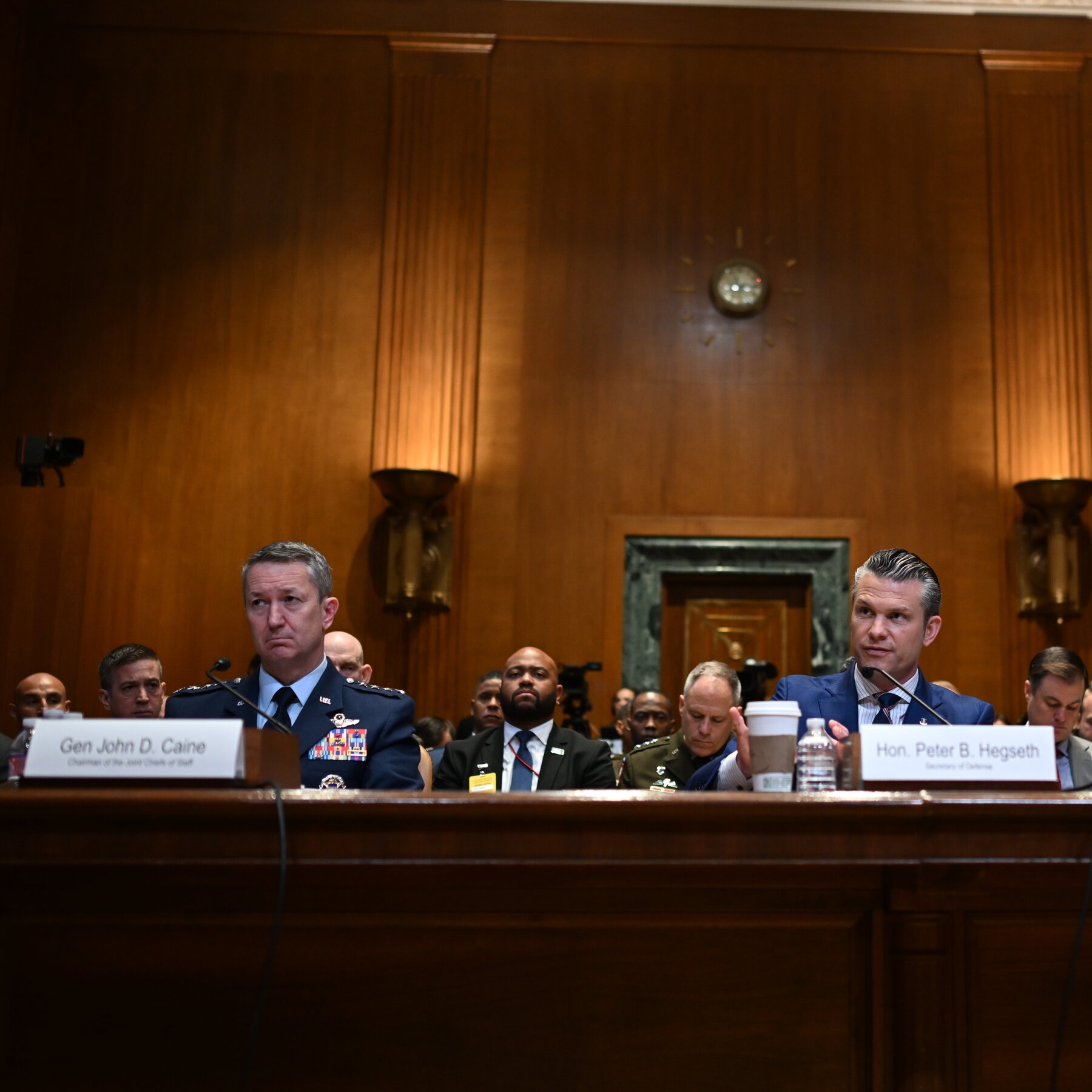 Two men seated before microphones in a wood-paneled room.