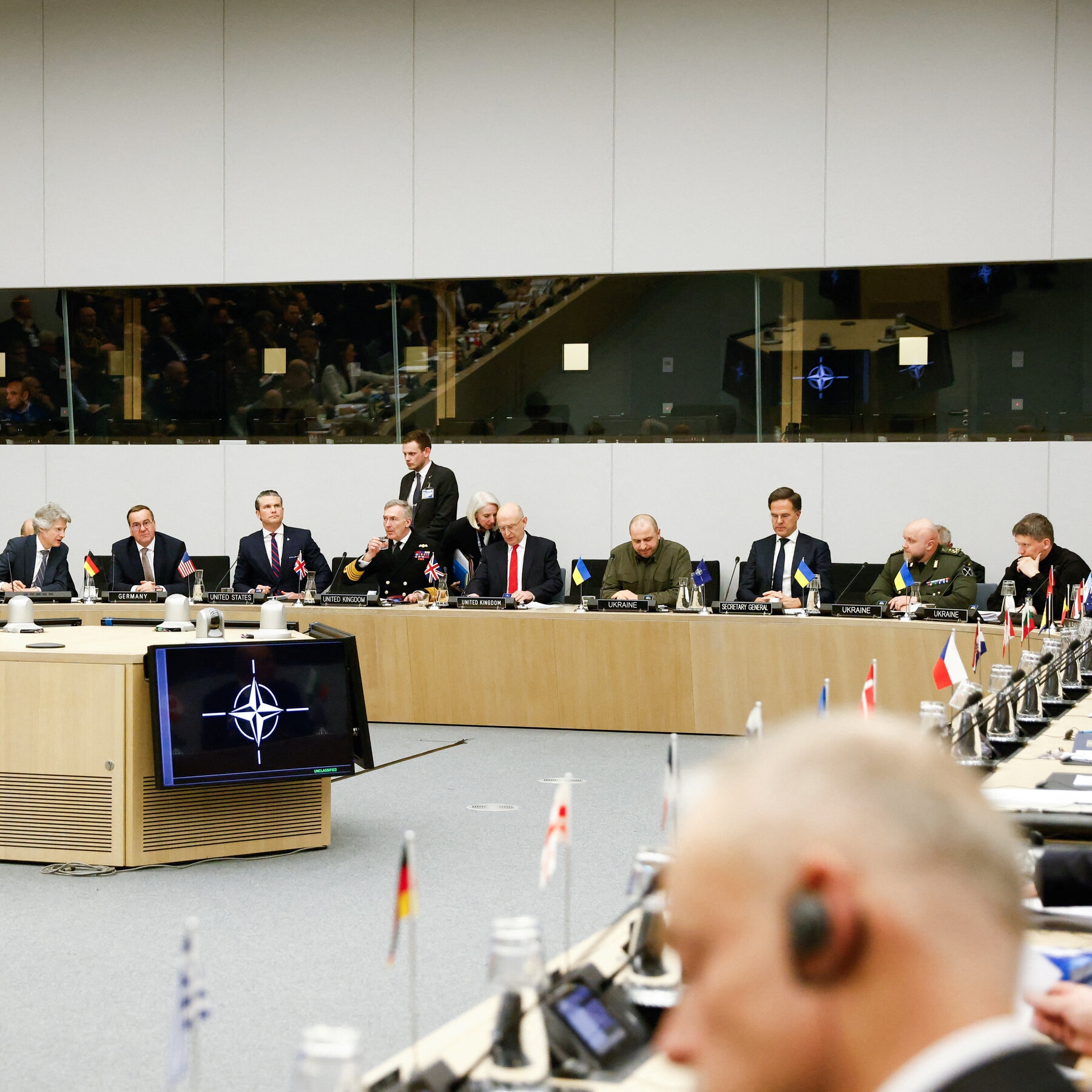 People seated with microphones along a large table circling a room.