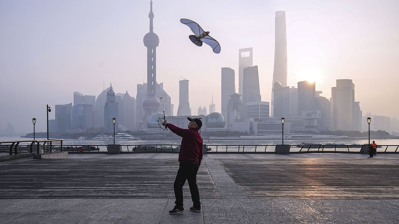 A man flies a kite on the Bund in front of buildings in Lujiazui Financial District, Shanghai, China