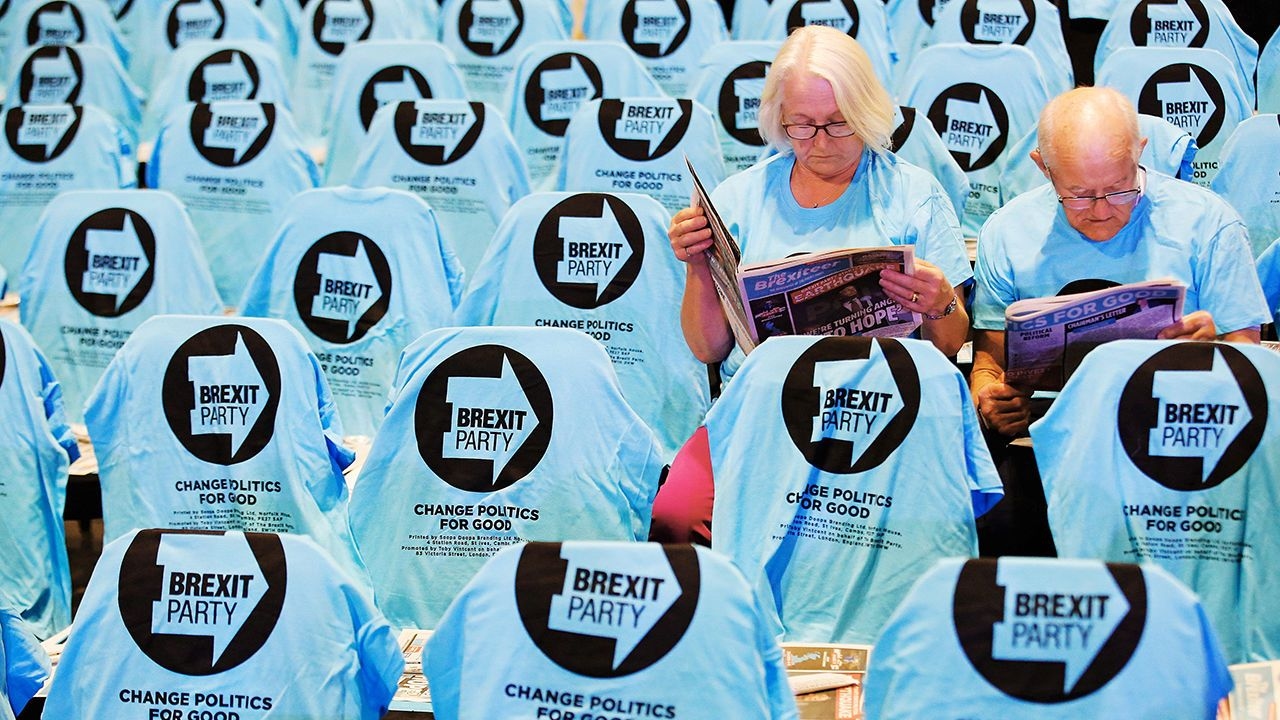 Supporters read copies of “The Brexiteer” party newspaper surrounded by empty seats. 
