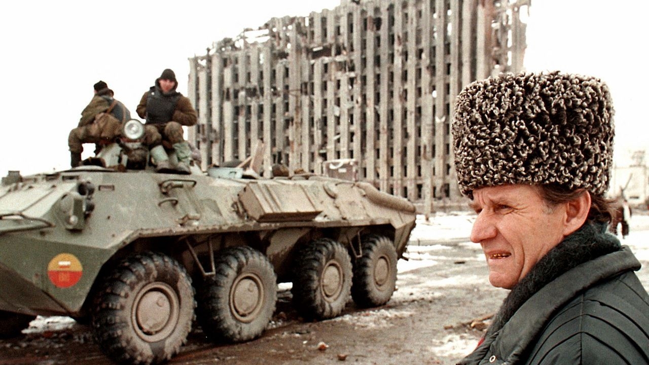 ussian soldiers a top of APC passing by a Chechen man in Grozny with the ruins of the Presidential palace in the background