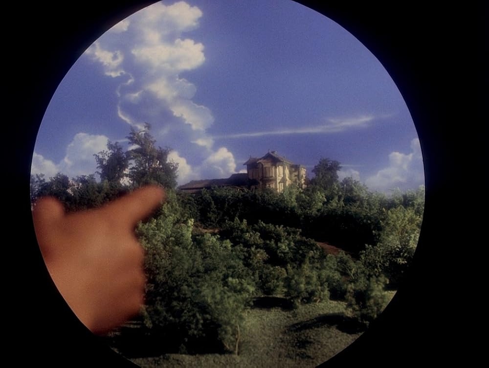 Чи є це радше іграшковою моделькою, на яку тицяють? Найімовірніше. Але цей простий кадр класний тим, що він умисне округлений, ще більше акцентуючи увагу на будинку. Він додає художности, бо всякі урізання оголюють факт, що це, в першу чершу, вигадка, кіно. 