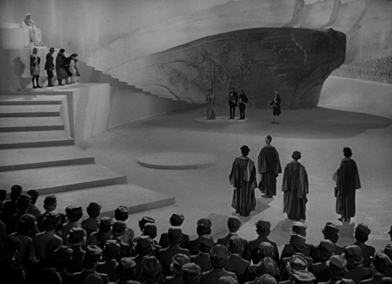 Небесний суд. Ви лишень оцініть красу цього кадру, де глибина йде не лишень зліва-внизу — справа угору, але й зліва-вниз — зліва-вгору і справа-вгору — зліва вгору. Яка постановка, всіх персонажів видко, позиції сили очевидні, а порожній центр — для сторони захисту, котрий ще на Землі. . 