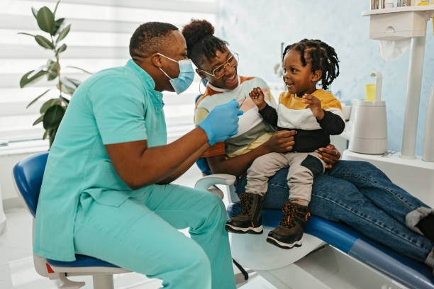 I am not afraid of the exam Doctor who is African American and wearing a mask is using dental tools to examine a child's teeth. The young person has no exam anxiety. family dentist stock pictures, royalty-free photos & images