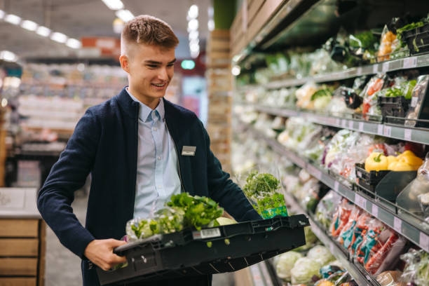 Shop assistant restocking the produce section shelves Shop assistant in supermarket re-stocking fresh vegetables in shelves of produce section. Part Time Job stock pictures, royalty-free photos & images