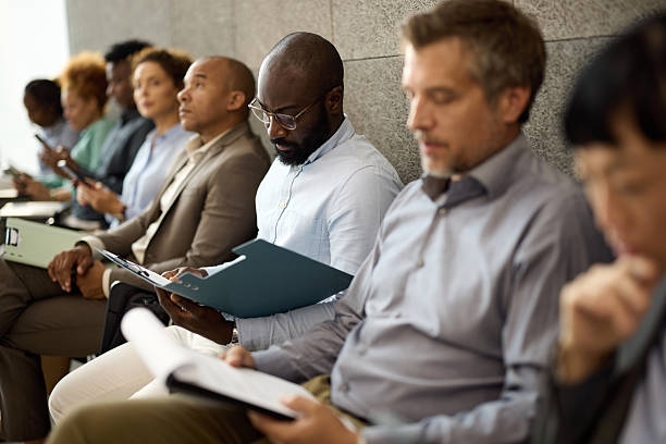 Black businessman reading resume while waiting for a job interview. African American male candidate reading his paperwork while waiting for job interview with other candidate in the office. Job Vacancy stock pictures, royalty-free photos & images