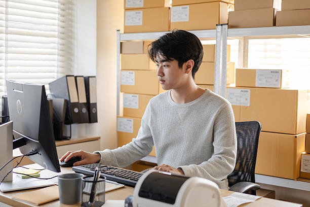Small business warehouse owner working at desktop computer managing ecommerce inventory and shipping orders in storage office. Small business warehouse owner working at desktop computer managing ecommerce inventory and shipping orders in storage office. Part Time Job stock pictures, royalty-free photos & images