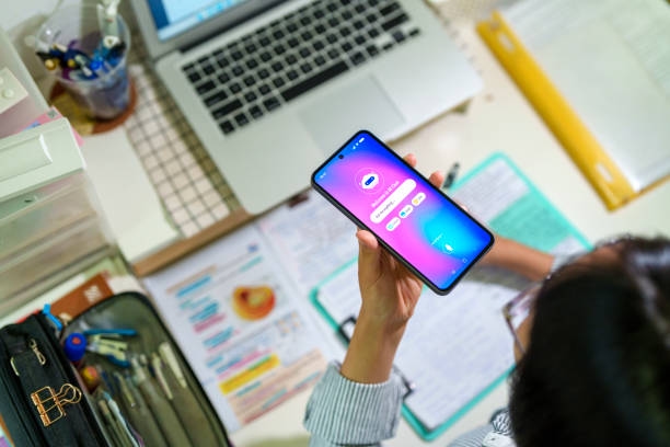 Student Using AI Chatbot While Studying An Asian teenage student interacts with an AI chatbot on a smartphone while studying at a desk with a laptop, notes and stationery. The scene highlights modern learning and technology integration. Customer Service Virtual Assistant stock pictures, royalty-free photos & images